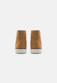 Brune kanvastøfler med høy topp og hvite gummisåler, med et enkelt design og glatt tekstur. Bakvinduet viser minimale stingdetaljer.