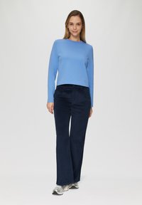 Lichtblauw lange mouwen top met een ronde hals, gecombineerd met donker marineblauwe corduroy wijde broek. Model draagt zilveren sneakers.