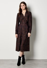 Abito a stampa leopardata con maniche lunghe, frontale con bottoni, lunghezza al ginocchio. Realizzato in un morbido tessuto nei colori nero e ruggine, abbinato a stivaletti neri.