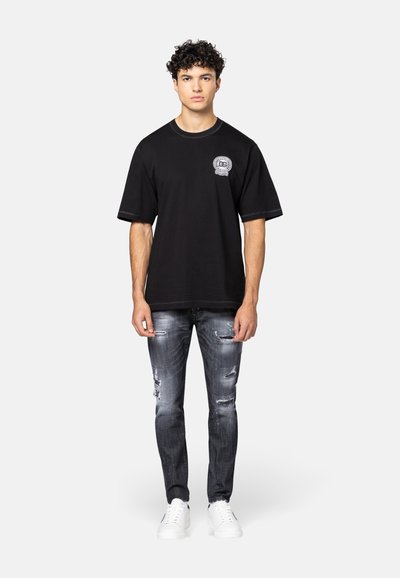 Zwarte katoenen T-shirt met een ronde hals, voorzien van een grafische afbeelding op de borst. G gedragen met versleten grijze jeans en witte sneakers.