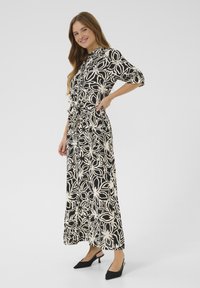 Robe maxi à motif floral noir et blanc avec une taille cintrée, un col boutonné et des manches 3/4. Portée avec des chaussures à talons noirs à coupe slingback.