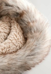 Tissu shearling beige doux enroulé à l'intérieur d'un anneau en fausse fourrure marron clair et grise.