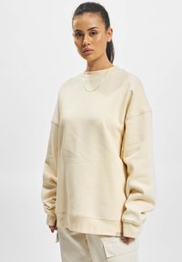 Sweatshirt oversized de culoare bej deschis, cu decolteu rotund, umeri căzuți și tiv zimțat. Material moale cu detalii minime.