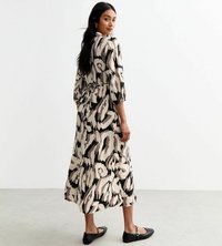 Maxikleid aus leichtem Stoff mit einem schwarz-beigen abstrakten Muster, Dreiviertelärmel, tailliertem Schnitt und flachen schwarzen Schuhen.
