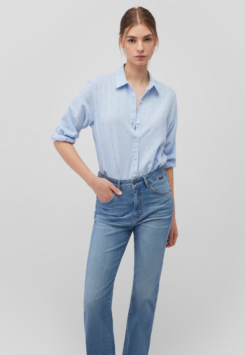 Hellblaue button-up Hemd mit einem gestickten Muster und hochgekrempelten Ärmeln, kombiniert mit hellblauen hochgeschnittenen Jeans.
