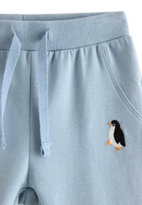 Vaaleansiniset collegehousut, joissa on resorivyötärö ja kiristysnauha, ja vasemmassa taskussa kirjailtu pingviinikuosi. Pehmeä tuntuma.