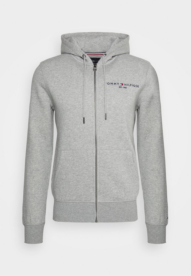Sweat à capuche zippé gris clair avec poches avant, cordon de serrage à la capuche et petit logo Tommy Hilfiger sur le côté gauche de la poitrine.