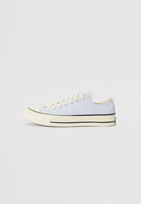 Baskets en toile bleu clair avec un embout en caoutchouc, des lacets crème et une bande noire le long de la semelle. Conception basse.