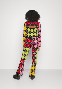 Conjunto de malha multicolorido e estampado com design argyle em vermelho, rosa, verde e amarelo. Detalhe nas costas em recorte com calças largas.
