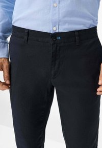 Donker marineblauwe broeken met een zachte textuur, voorzien van een knoopsluiting en riemlussen. Gecombineerd met een lichtblauw overhemd met knopen.