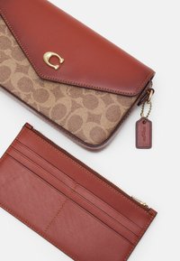 Hnědá kožená peněženka s texturovaným béžovým vzorem, zlatými doplňky a štítkem. Pod ní se nachází menší odpovídající peněženka s přihrádky na karty a zipem.