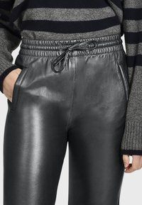 Zwarte leren joggers met een elastische tailleband, koord en zijzakken. Glad oppervlak met een glanzende afwerking.