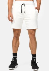 Hvide shorts i bomuldsblanding med snoretræk i taljen og lommer. Har en glat overflade og oprollende kanter. Kombineret med sorte sneakers og sokker.