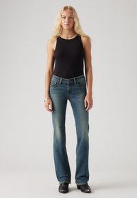 Black sleeveless top paired with blue flared jeans. The jeans feature a classic five-pocket design and subtle fading. Black boots complete the look.