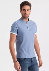 Svetle modré polo tričko s krátkým rukávem a henley límcem, bílé akcenty na rukávech a malé logo na lemu. Hladká textura.