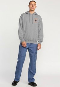 Gray hoodie with front pocket and drawstring, paired with blue cargo pants featuring multiple pockets and a relaxed fit. Black shoes.