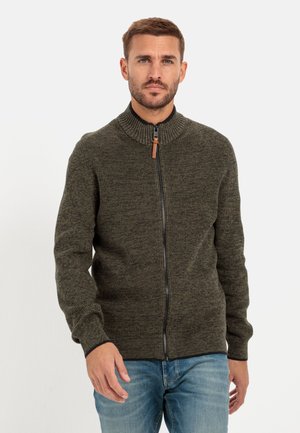 Grüner, gestrickter Reißverschluss-Pullover mit hohem Kragen, gerippter Textur und Leder-Zipper. Getragen mit hellblauen Jeans.