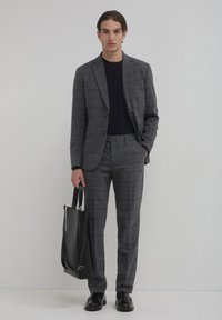 Grau kariertes Anzug mit einem maßgeschneiderten Blazer und schmal geschnittenen Hosen, kombiniert mit einem schwarzen Hemd und einer schwarzen Tote-Tasche. Glatte Stoffe und elegantes Design.