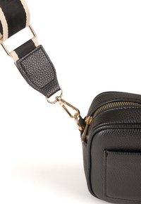 Sac en cuir noir à bandoulière avec une finition texturée, des accessoires en métal doré et une sangle en tissu rayée amovible. Forme carrée compacte.