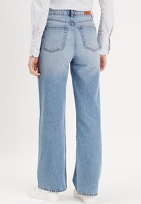 Jeans en denim bleu clair, �à pattes larges, avec une taille haute, comportant deux poches arrière, un ourlet effiloché et un léger délavage sur les cuisses.
