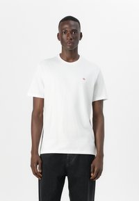 Witte katoenen t-shirt met een ronde hals, korte mouwen en een klein rood logo op de borst, gecombineerd met zwarte jeans.