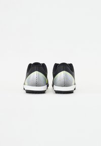 Zapatillas deportivas negras con una parte superior texturizada en negro, acentos reflectantes plateados y detalles en verde en el talón. Diseño perforado en los lados.