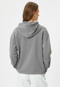 Sudadera gris con capucha de corte relajado, mangas largas y puños acanalados. El material parece suave, con una textura lisa y un detalle mínimo.