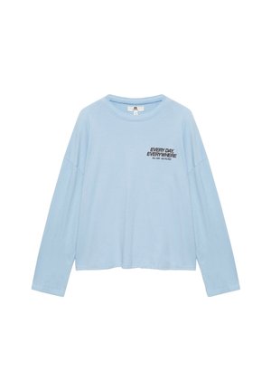 Chemise bleu clair à manches longues avec col rond et texte noir sur la poitrine indiquant "EVERY DAY EVERYWHERE ALL DAY - NO FILTER".