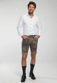 Witte lange mouw shirt met brown knopen, gedragen met bruine leren shorts met borduursels en een gestreepte zwarte riem, aangevuld met zwarte schoenen en donkere sokken.