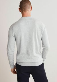 Szary sweatshirt z długimi rękawami, ściągaczami przy mankietach i pasie. Gładka tekstura, klasyczny krój z okrągłym dekoltem oraz prosty, minimalistyczny wygląd.