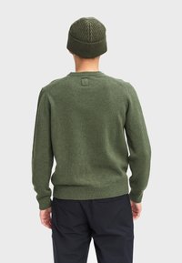 Maglione verde a maglia con maniche lunghe e colletto a coste, abbinato a un berretto coordinato con coste, indossato con pantaloni scuri.