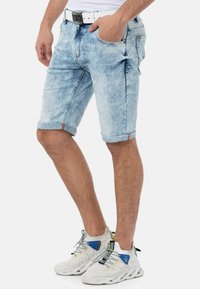 Helle blaue Denim-Shorts mit einem verblassten Finish, umgeschlagenen Säumen und Taschen vorne und hinten. Getragen mit weißen Sneakers mit blauen Akzenten.