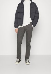 Czarna kurtka puchowa, biała sweterkowa bluzka, szare spodnie, czarno-białe trampki. Kurtka puchowa ma wysoki kołnierz i pikowaną strukturę.