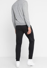 Felpa grigia a maniche lunghe, scollo rotondo, abbinata a pantaloni jogger neri a gamba affusolata. Sneakers bianche completano l'outfit casual.
