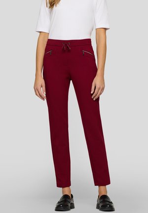 Burgunderfarbene Hose aus einem weichen Stoff, mit einem Kordelzugbund, Reißverschlusstaschen und schlankem Schnitt, kombiniert mit schwarzen Schuhen.