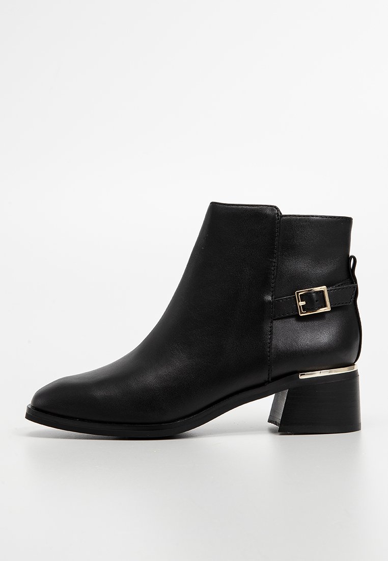 Botte noire à cheville en cuir lisse avec un bout arrondi, dotée d'une boucle sur le côté et d'un petit talon carré avec un accent métallique.
