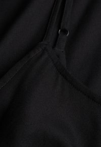 Sort stof med synlige sømme og en smal strop med en lille sølvring som vedhæng.