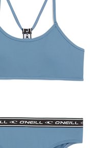 Sports bra blu con banda larga e logo nero sul fondo; presenta sottili spalline incrociate. Tessuto morbido ed elastico con texture liscia.