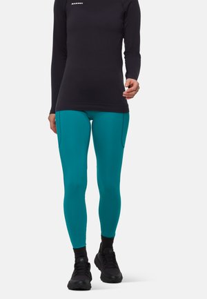 Leggings turchesi realizzati in tessuto elasticizzato, con un fit slim e tasche laterali, abbinati a una maglia nera a maniche lunghe e scarpe nere.