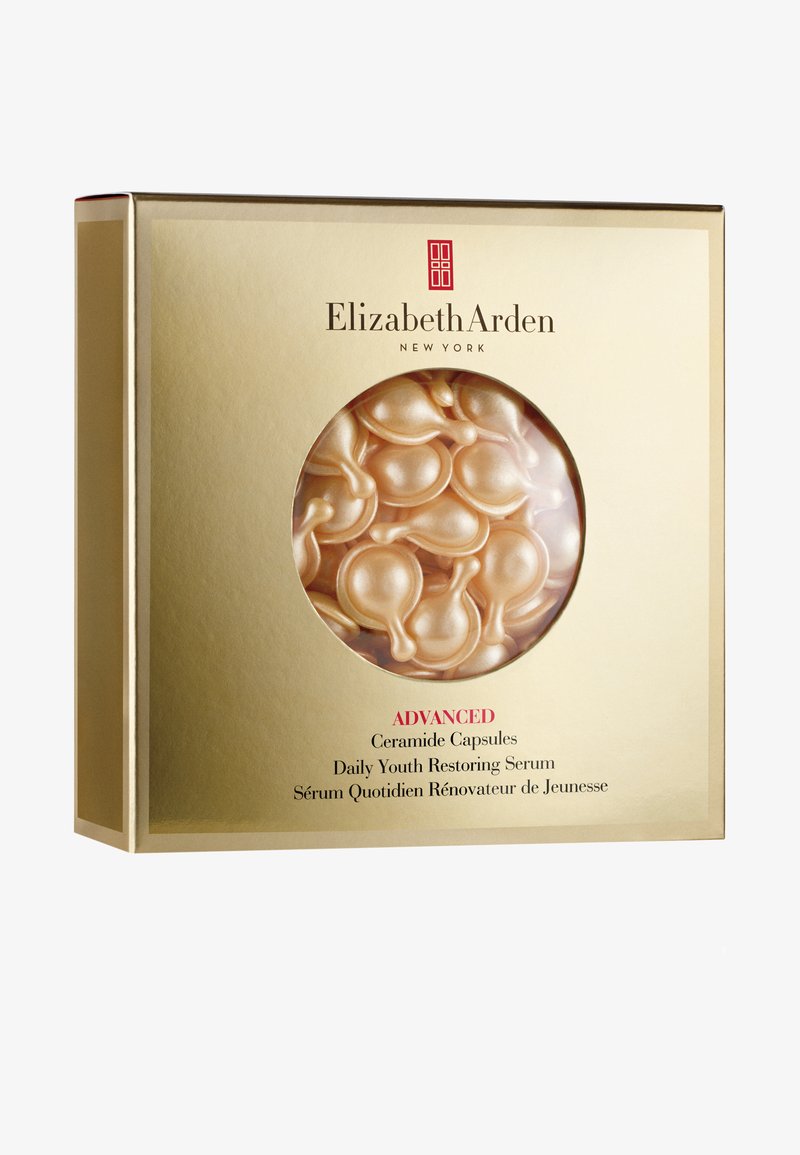 En guldig låda med ett runt fönster som avslöjar mjuka, persikofärgade kapslar. Innehåller text som anger produktnamn och fördelar i rött och svart.