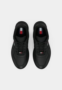 Paire de baskets noires à lacets avec le logo Tommy Jeans sur la languette et le côté, vues du dessus sur fond uni.