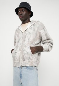 Lichte grijze zip-up hoodie met loofpatroon, heeft zakken, een zachte textuur en een comfortabele pasvorm, gecombineerd met lichtblauwe jeans.