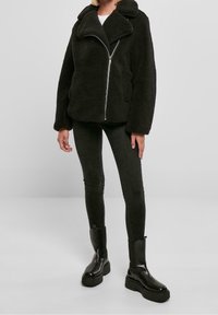 Sort, fluffy sherpa-jakke med bredt revers, frontlynlås og to sidelommer. Kombineret med mørke, stramme jeans og chunky sorte støvler.