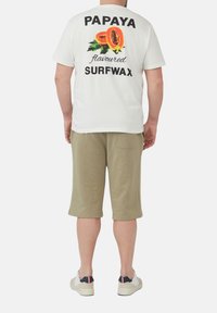 Witte katoenen t-shirt met een kleurrafische papaya en de vetgedrukte tekst "PAPAYA Smaken SURFWAX" op de rug; gecombineerd met khaki shorts.