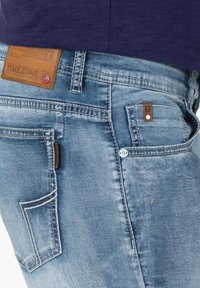 Lichtblauwe denim jeans met een vervaagd textuur. Kenmerken zijn onder andere een bruine leren label, vijf zakken en kenmerkende stiksels.