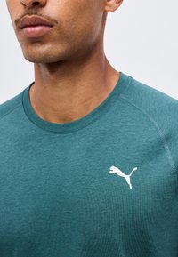 Άνδρας με μπλουζάκι Puma σε τιρκουάζ χρώμα με στρογγυλή λαιμόκοψη που δείχνει μερικώς το πρόσωπο και το πάνω μέρος του στήθους.