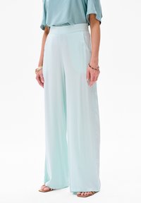 Lichtblauwe wide-leg broek gemaakt van een zachte, gladde stof met zijzakken en een hoge tailleband, gecombineerd met open teen sandaal.