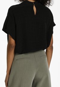 Haut noir tissé avec un détail dos en forme de goutte et manches courtes, associé à un pantalon gris taille haute avec une poche arrière unique.