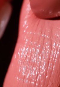 Pfirsichfarbener Lippenstift auf strukturierter Haut mit glänzendem Finish. Das Licht reflektiert auf der Oberfläche und hebt feine Linien sowie einen dezenten Glanz hervor.