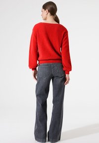 Pull rouge duveteux avec un col large et des épaules tombantes, associé à un jean taille haute, gris foncé et à jambes larges. Finition texturée sur l'ensemble.